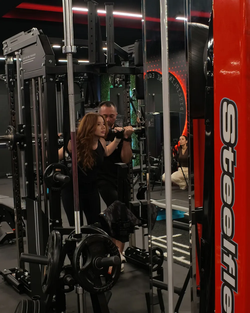Elevate Personal Training Gym Oman 34 Client on the Smith machine with her coach beside her at Elevate Azaiba